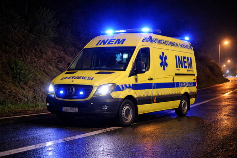 Ambulância do INEM em operação noturna com luzes de emergência ligadas.